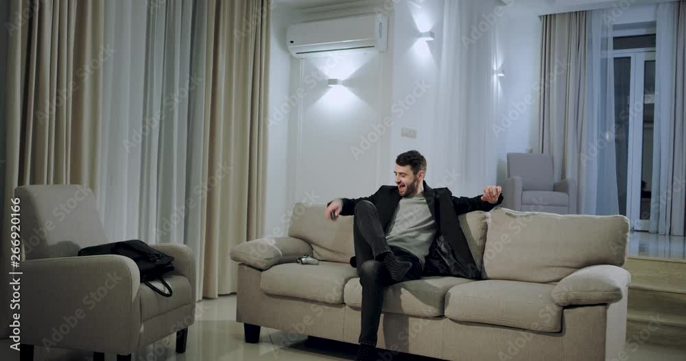 Young businessman come at home after a hard work day he comes in a large spacious living room take the PSP remote and starting to play a game to relaxing Young businessman come at home after a hard work day he comes in a large spacious living room take the PSP remote and starting to play a game to relaxing