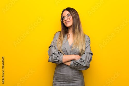 Young woman with glasses over yellow wall looking up while smiling