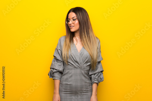 Young woman with glasses over yellow wall is a little bit nervous and scared pressing the teeth