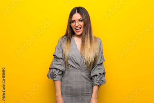 Young woman with glasses over yellow wall with surprise and shocked facial expression