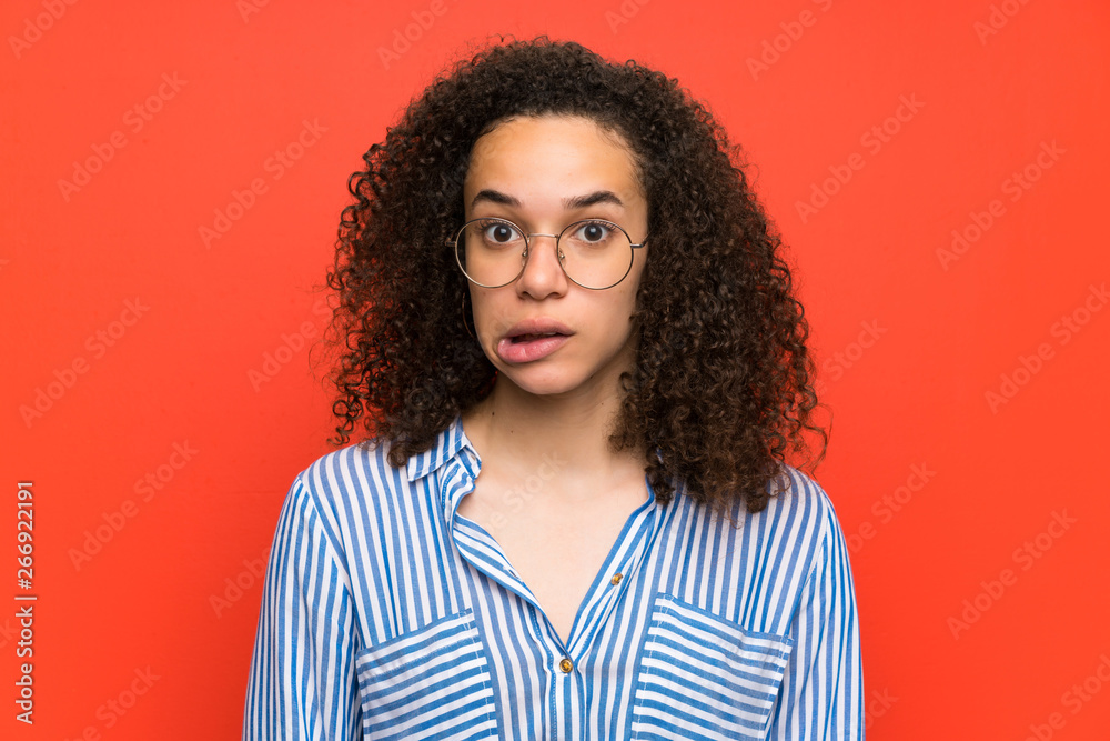 Dominican woman over red wall having doubts and with confuse face expression Dominican woman over red wall having doubts and with confuse face expression