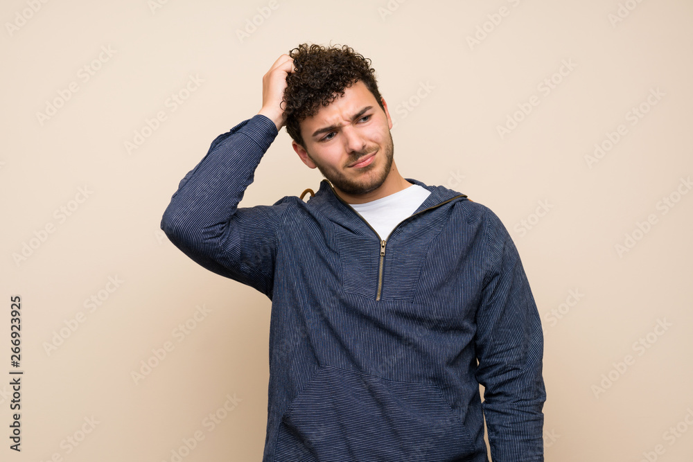Man with curly hair over isolated wall having doubts while scratching head Man with curly hair over isolated wall having doubts while scratching head