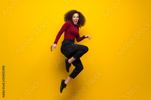 Fototapeta Naklejka Na Ścianę i Meble -  Dominican woman with curly hair jumping over isolated yellow wall