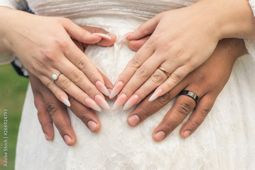 Pregnant newlywed woman, with husband embracing from behind, with their hands placed over her belly in a white dress. Close up conceptual view of love and bonding during pregnancy Pregnant newlywed woman, with husband embracing from behind, with their hands placed over her belly in a white dress. Close up conceptual view of love and bonding during pregnancy