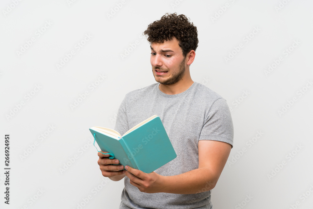 Man with curly hair over isolated wall holding and reading a book Man with curly hair over isolated wall holding and reading a book