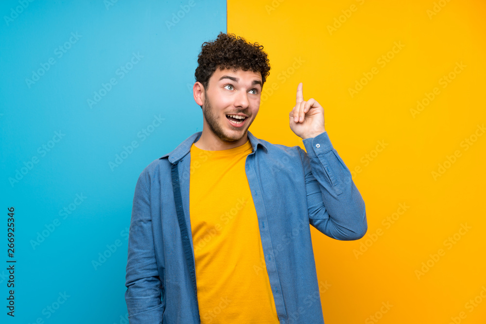 Man with curly hair over colorful wall intending to realizes the solution while lifting a finger up Man with curly hair over colorful wall intending to realizes the solution while lifting a finger up
