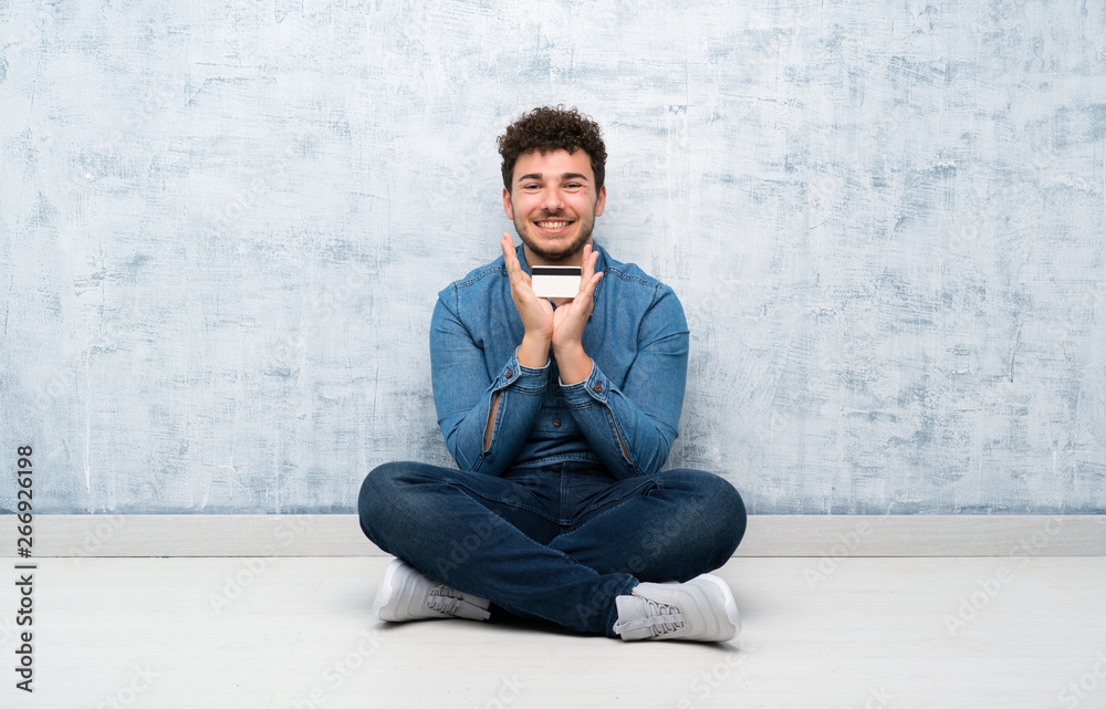 Young man sitting on the floor holding a credit card Young man sitting on the floor holding a credit card