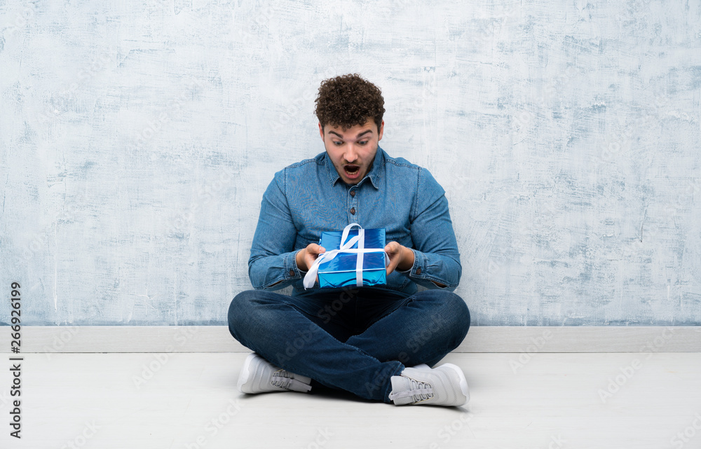 Young man sitting on the floor holding gift box Young man sitting on the floor holding gift box