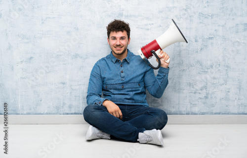Young man sitting on the floor holding a megaphone