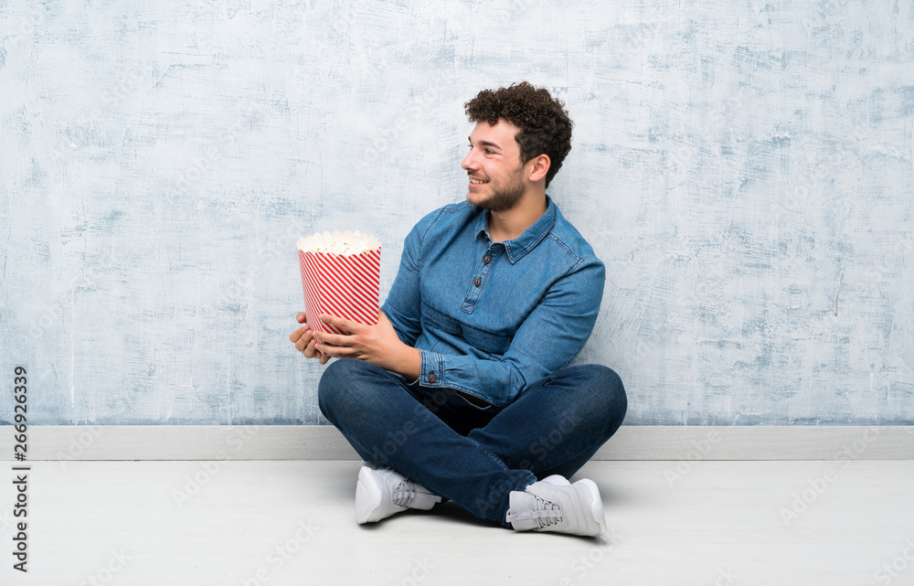 Young man sitting on the floor holding a bowl of popcorns Young man sitting on the floor holding a bowl of popcorns