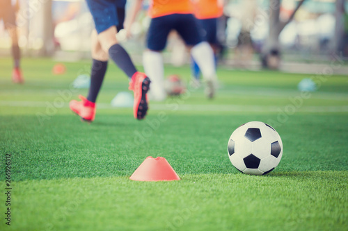 Fototapeta Naklejka Na Ścianę i Meble -  football between marker cones on green artificial turf with blurry soccer team training