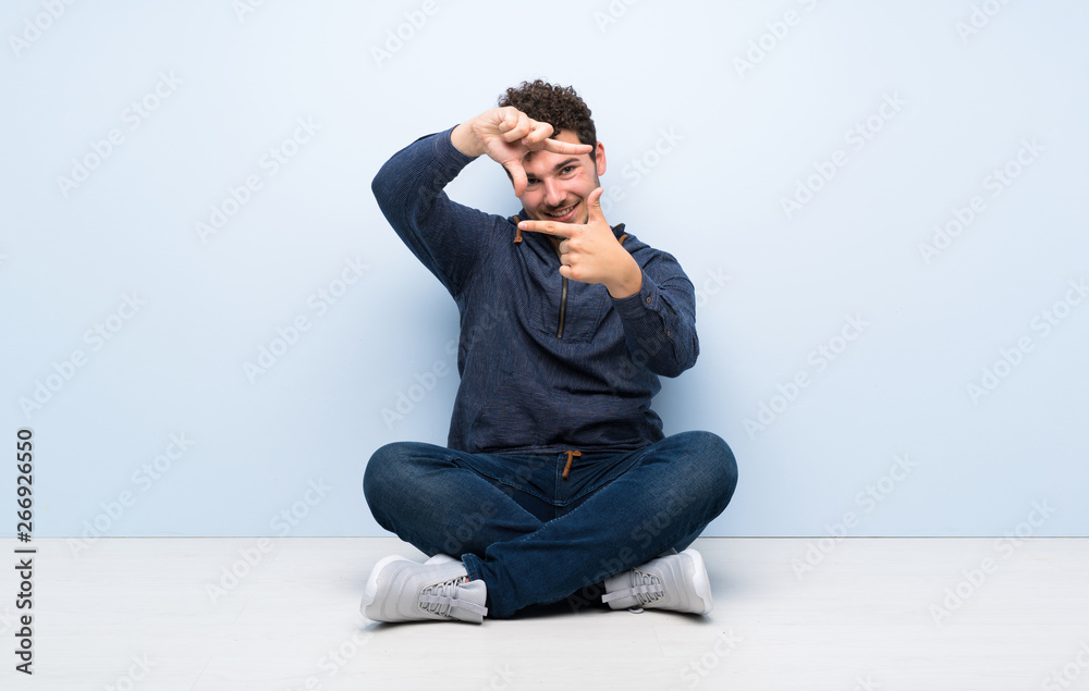 Young man sitting on the floor focusing face. Framing symbol Young man sitting on the floor focusing face. Framing symbol