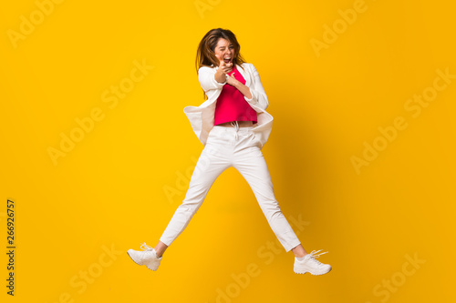 Young woman jumping over isolated yellow wall pointing to the front