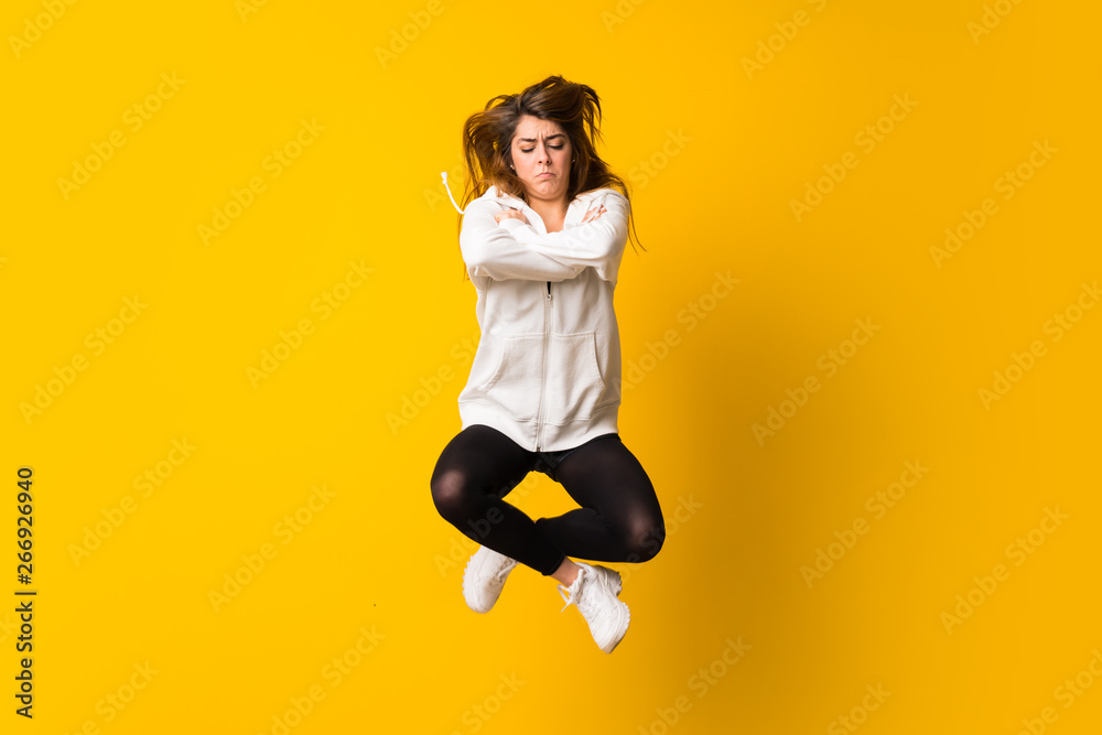 Sad Young woman jumping over isolated yellow wall