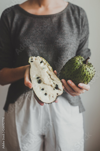 the girl keeps a Soursop fruit or graviola. A young woman holds an guyabano in her hands on a grey background