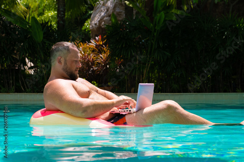 Male freelancer with a laptop on rubber ring in the water