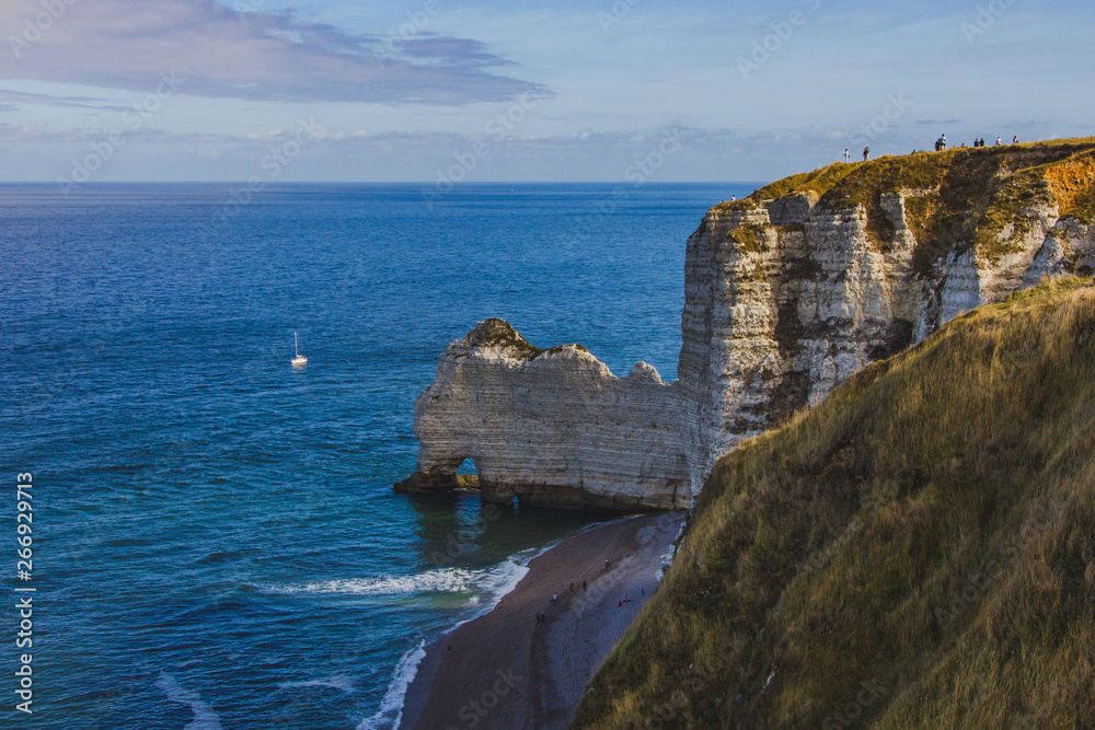 Beautiful famous chalk cliffs of Aval Etretat, skyline with blue sky and ocean water with sailboat, Normandy, France, Europe, top view