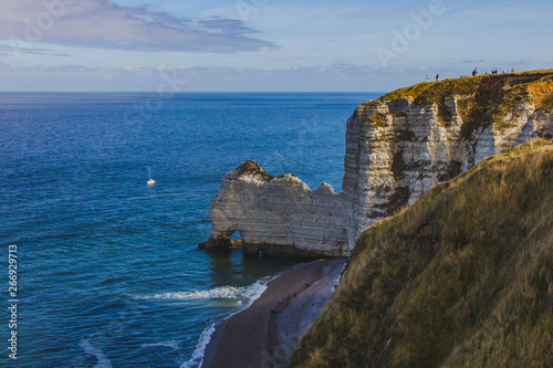 Beautiful famous chalk cliffs of Aval Etretat, skyline with blue sky and ocean water with sailboat, Normandy, France, Europe, top view