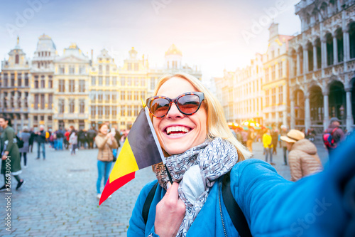 Woman tourist stands with the flag of Belgium on the background of the Grand-Place or the Grand Market Square in Brussels