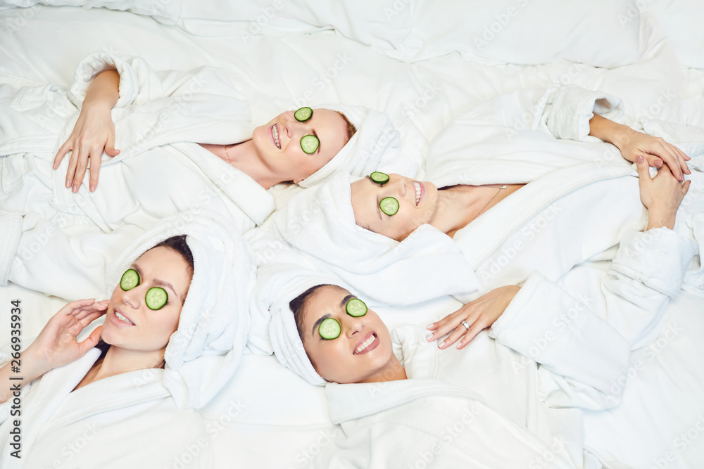 Chilling women in bathrobes with cucumber slices on face Chilling women in bathrobes with cucumber slices on face
