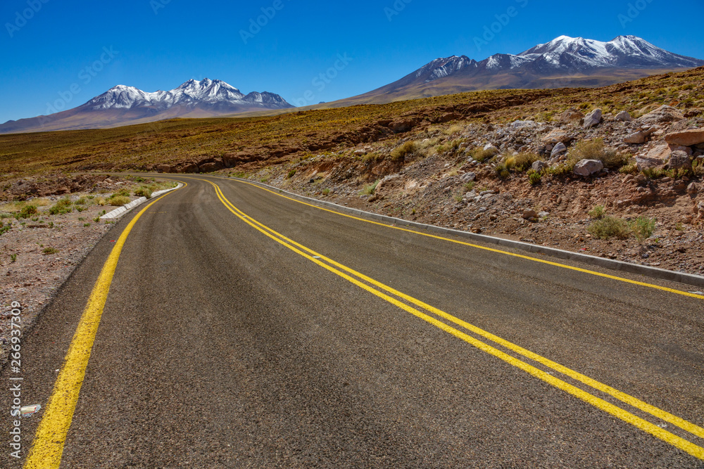Atacama curved road and snow covered volcanoes