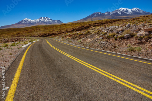 Atacama curved road and snow covered volcanoes