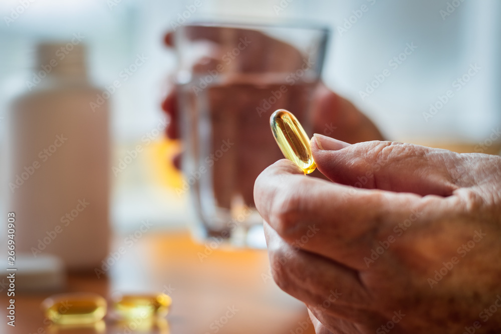 Senior woman holding omega-3 fish oil nutritional supplement and glass of water