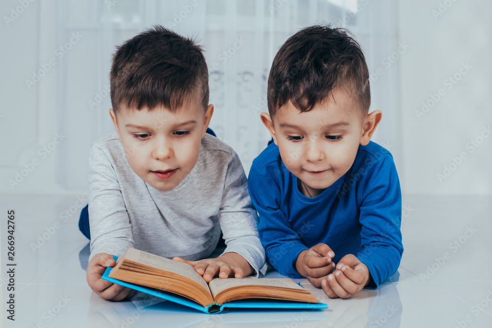 Photo of two charming boys, brothers or friends, lying on the floor smiling happily reading a book. Photo of two charming boys, brothers or friends, lying on the floor smiling happily reading a book.