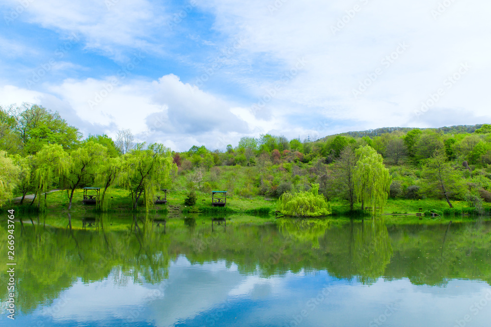 wooden gazebos and weeping willows on the lakeshore in a clear sunny day and their reflection in the lake wooden gazebos and weeping willows on the lakeshore in a clear sunny day and their reflection in the lake