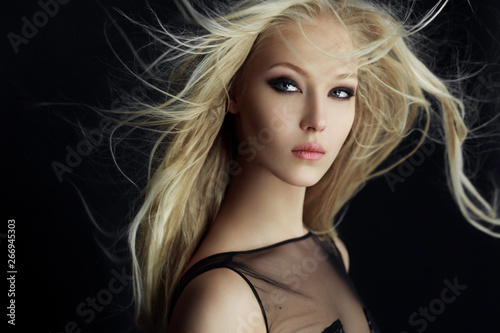 Graceful blonde girl in perfect make up with hair scattered by the wind, isolated on a black background. photo