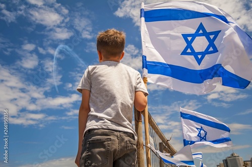Israeli kid watching the aviation show on the 71 Israel Independence Day with a flag of Israel against the blue sky.