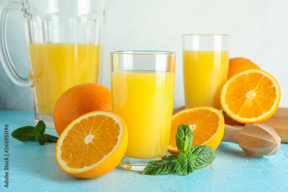 Composition with fresh orange juice in glassware, mint and wooden juicer on color table against white background, closeup. Fresh natural drink Composition with fresh orange juice in glassware, mint and wooden juicer on color table against white background, closeup. Fresh natural drink