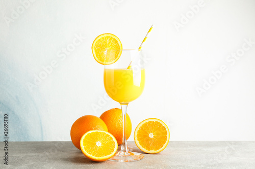 Glass with fresh orange juice and tubule, oranges on grey table against color background, space for text. Fresh natural drink