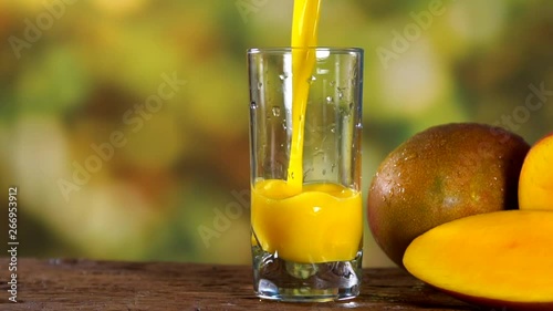 Mango juice pouring in a glass with tree blurry background . Preparing juice. Slow motion.