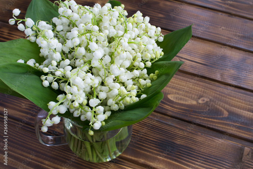 Bouquet of lily of the valley  in the glass jug on the brown wooden  background.Top view.Spring flowers concept.