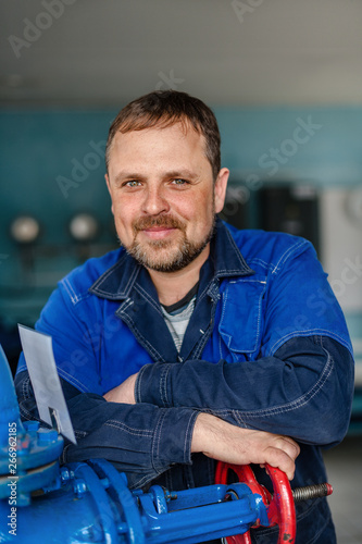 Portrait of a locksmith in the boiler room at the workplace. A white man with a beard with kind eyes looks into the camera and smiles