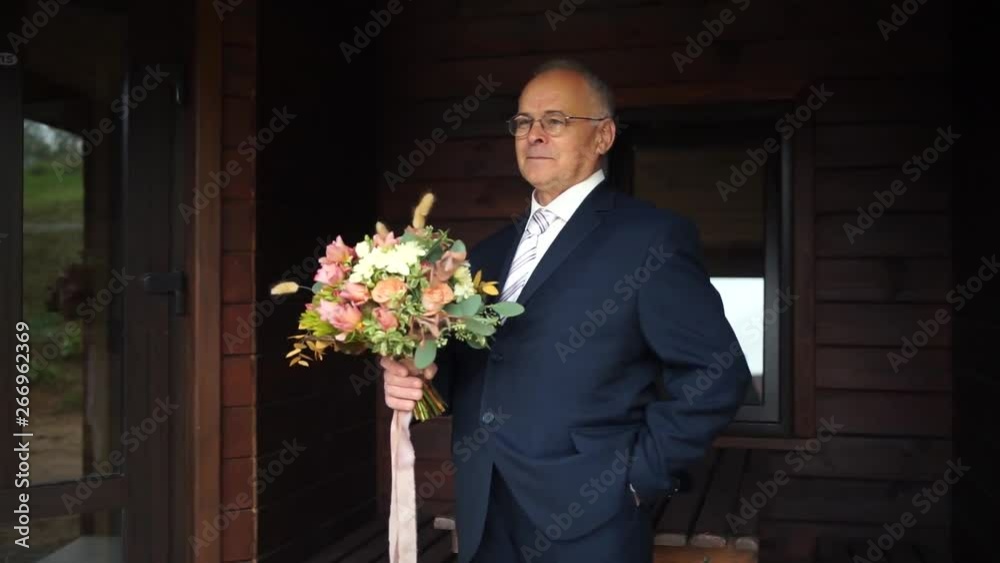 An elderly man holding a bouquet of roses. Old man suit holding flowers. The old man smiles at the camera. An elderly man holding a bouquet of roses. Old man suit holding flowers. The old man smiles at the camera.