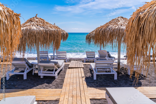 Fototapeta Naklejka Na Ścianę i Meble -  Empty deck chairs and umbrellas on the black sand beach in Perissa, Santorini, Greece