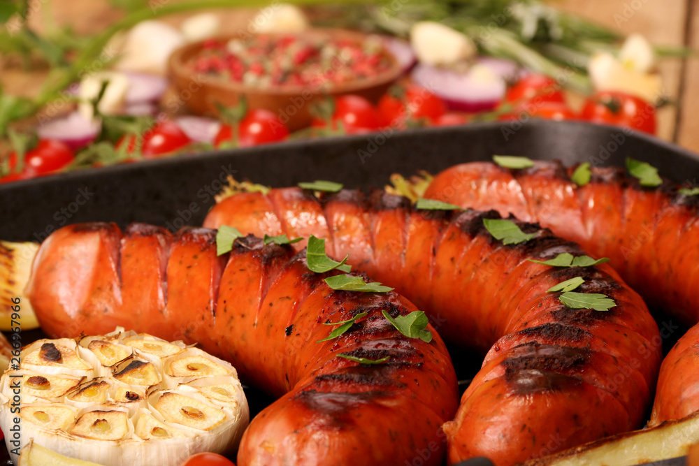 Grilled sausages with vegetables and spices in a pan on wooden background Grilled sausages with vegetables and spices in a pan on wooden background