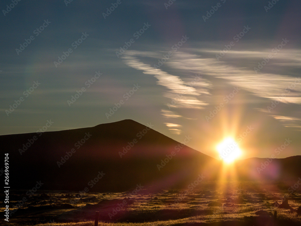 A morning sun rising above the mountains, leaving the whole region in darker shades, absorbing all the energy and colors. Few clouds on the sky.