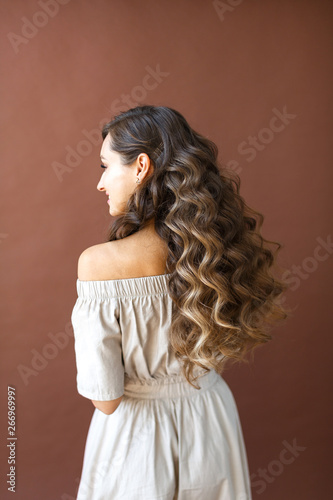 Young beautiful brunette woman is standing back, wave hairstyle, long female hair