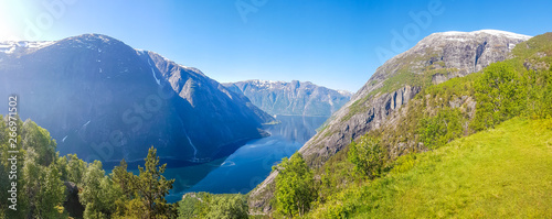 An majestic view on Eidfjord from Kjeasen, Norway. Slopes of the mountains are overgrown with lush green grass. Water has dark blue color. Taller parts of the mountains are barren. Sunny and clear day photo