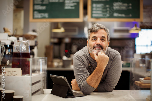 Quadro su tela Portrait of owner with tablet computer leaning on counter in cafe