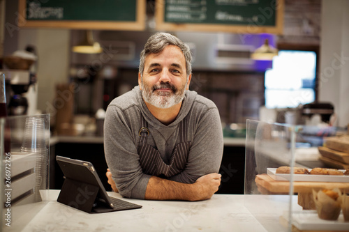 Canvas Print Portrait of smiling male owner with tablet computer on bar counter standing in c