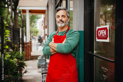 Картината върху платно Portrait of male entrepreneur with arms crossed standing by open sign at cafe