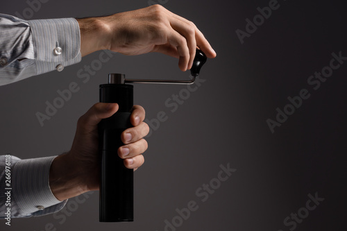 A man grinds grain coffee with a manual coffee grinder. Dark background