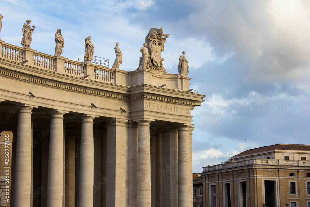 Roof of Saint Peter's Cathedral in the Vatican with various statues and sculptures on it, columns below and cathedral's dome above and on the right. Vatican, Rome, Italy