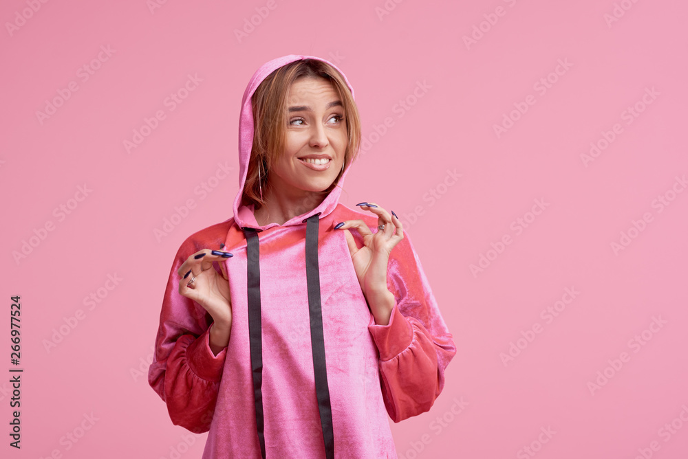Portrait of a cheerful young girl in pink hoodie clothes looking at camera and winking isolated over pink background Portrait of a cheerful young girl in pink hoodie clothes looking at camera and winking isolated over pink background