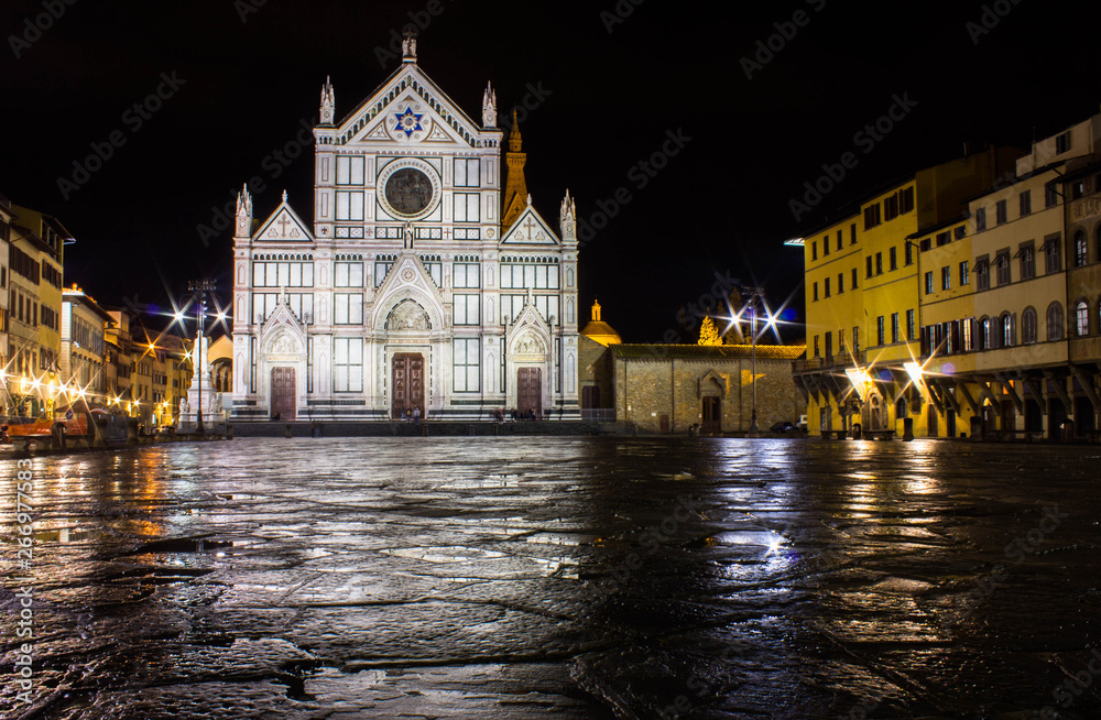 Night photo, illuminated cathedral Santa  Croce, wet after rain ground of square (piazza) reflecting church facade and nearby residential buildings. Long exposure photography.