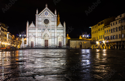 Night photo, illuminated cathedral Santa Croce, wet after rain ground of square (piazza) reflecting church facade and nearby residential buildings. Long exposure photography.